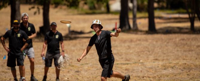 An image of man playing disc golf while three men watching